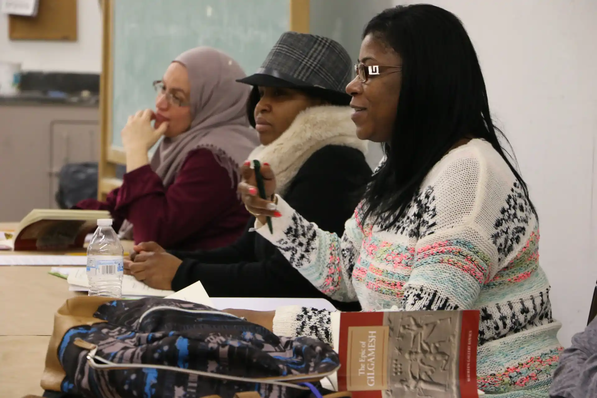 Three adult students seated at a seminar table, one speaking while the others listen.